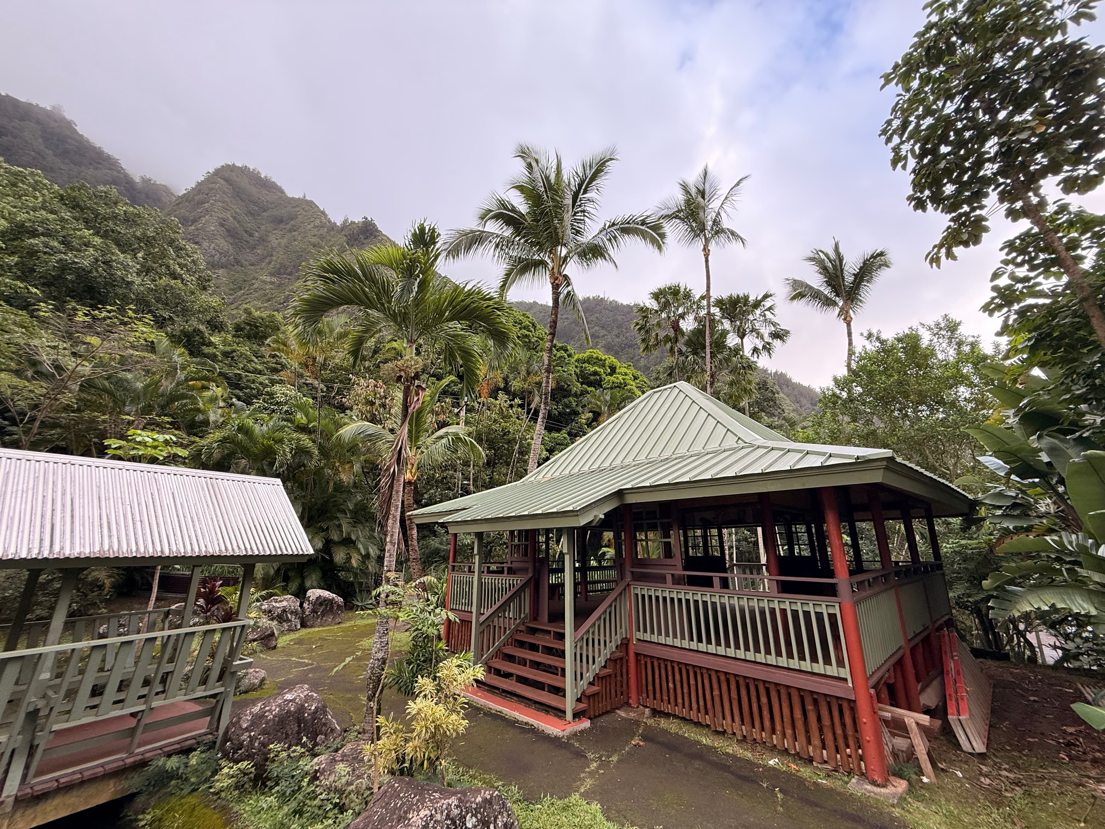 Bahay kubo pavilion with green roof nestled among palms and misty forested mountains