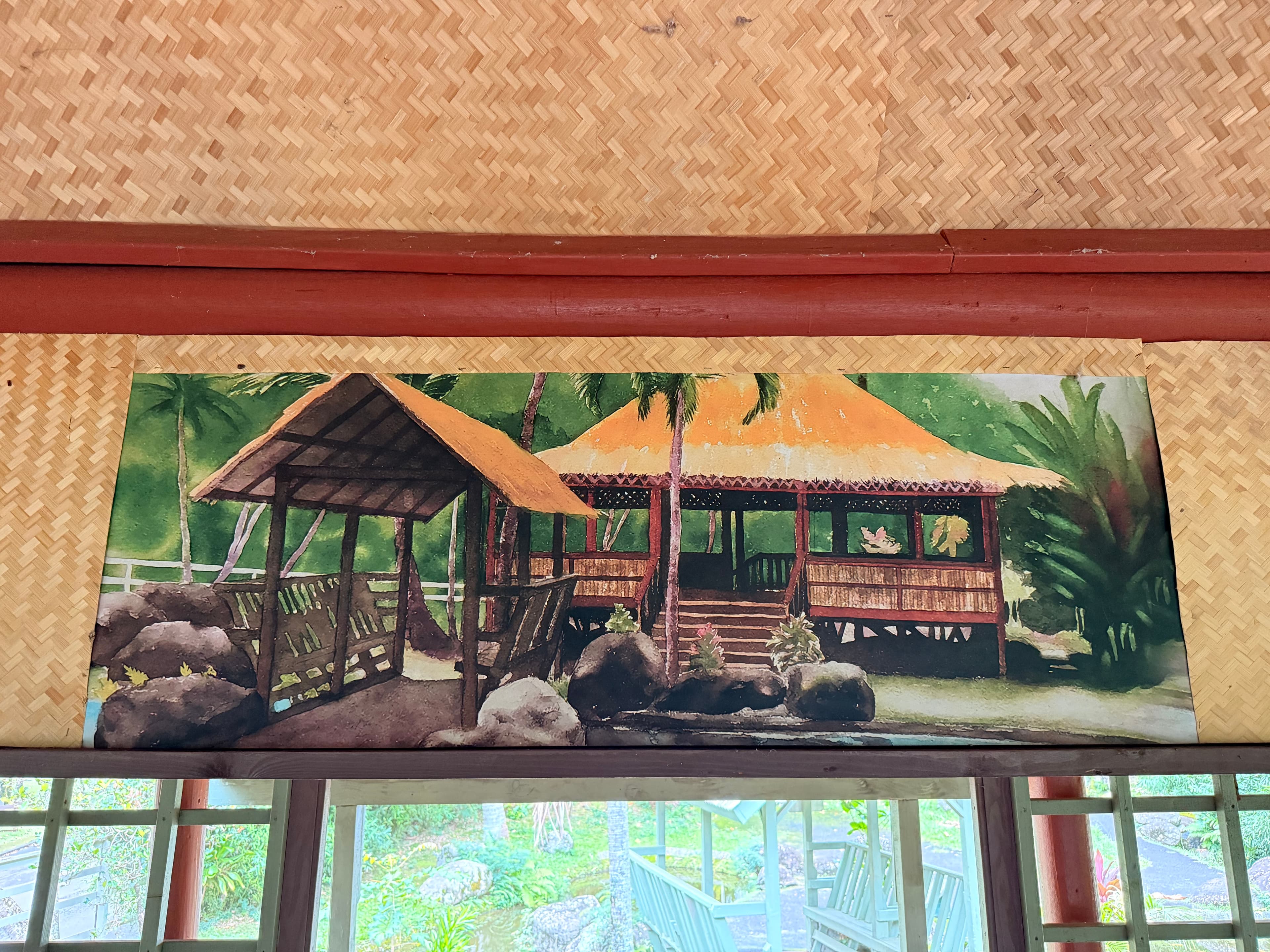 Watercolor painting of two bahay kubo with thatched roofs among tropical plants, mounted on a woven bamboo wall